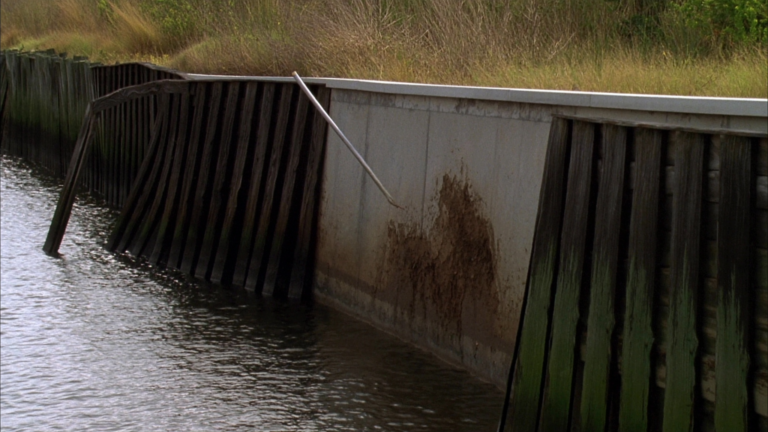 Failing timber bulkhead leaning on a Charleston waterfront with soil washing out behind it